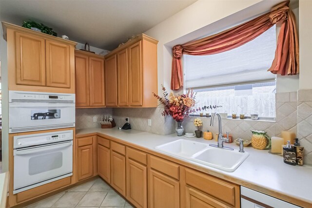 kitchen with light countertops, white double oven, tasteful backsplash, and a sink