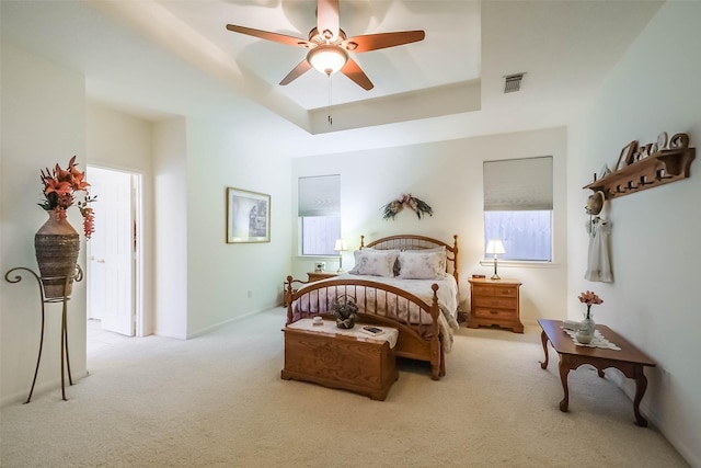 carpeted bedroom with ceiling fan, a tray ceiling, and visible vents