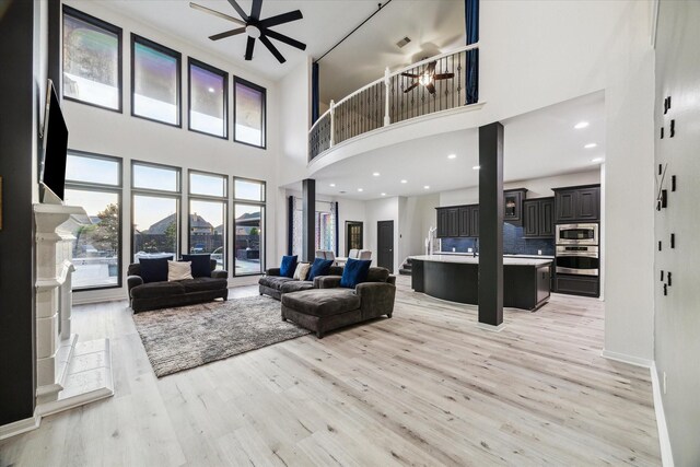 living room featuring baseboards, ceiling fan, light wood-type flooring, and a towering ceiling