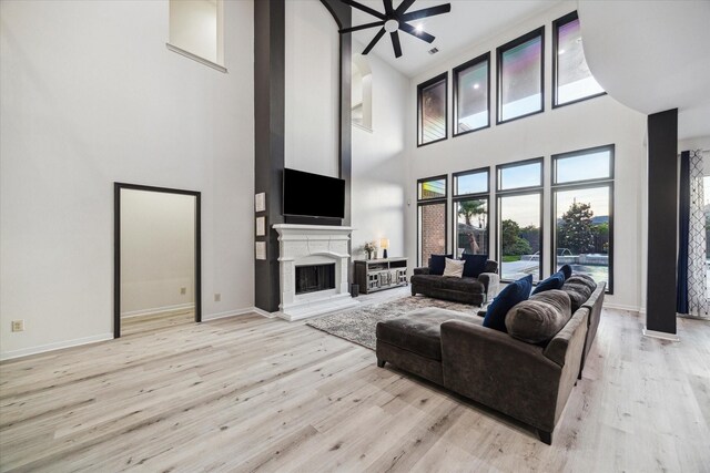 living room featuring a fireplace with raised hearth, light wood finished floors, ceiling fan, and a high ceiling