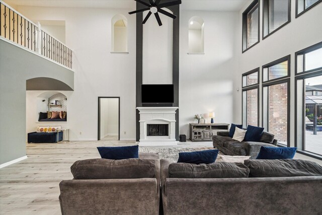 living room with a ceiling fan, wood finished floors, baseboards, a fireplace with raised hearth, and a high ceiling
