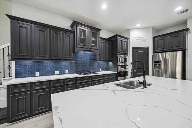 kitchen with a sink, dark cabinets, stainless steel appliances, backsplash, and visible vents