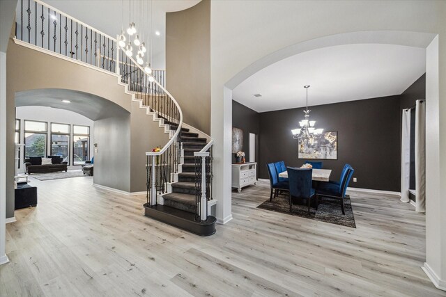 entrance foyer with arched walkways, stairs, wood finished floors, and a notable chandelier