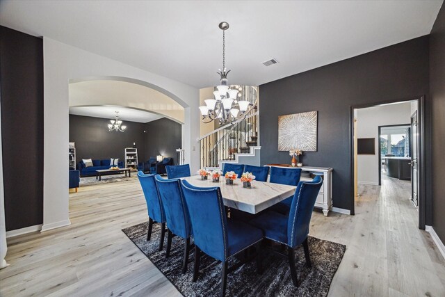 dining space featuring visible vents, arched walkways, stairway, a chandelier, and light wood-style flooring