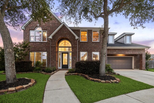 traditional-style house featuring brick siding, an attached garage, driveway, and a front lawn