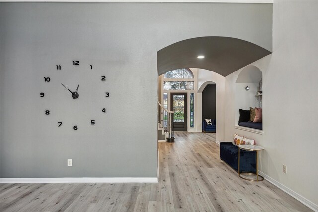 foyer entrance featuring arched walkways, baseboards, light wood finished floors, and stairs