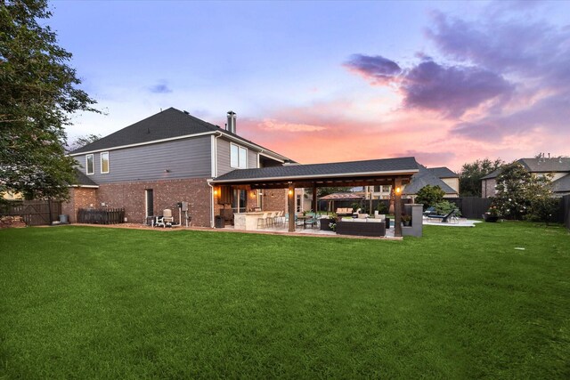 back of house at dusk with a yard, a patio, an outdoor living space, and a fenced backyard