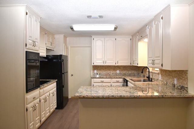 kitchen featuring tasteful backsplash, wood finished floors, a sink, black appliances, and a peninsula