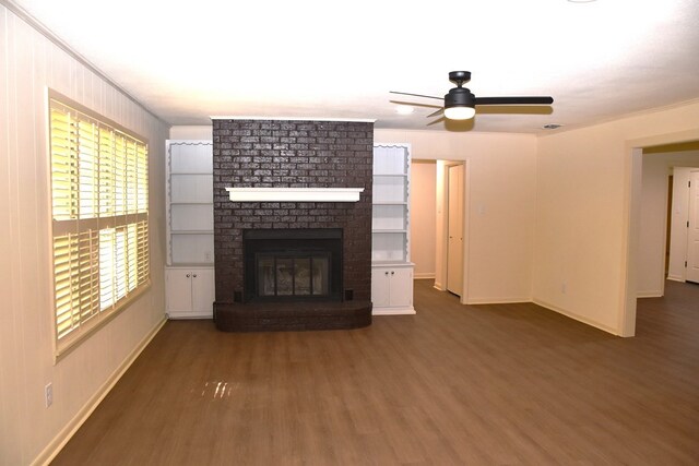 unfurnished living room featuring baseboards, wood finished floors, a brick fireplace, ceiling fan, and ornamental molding