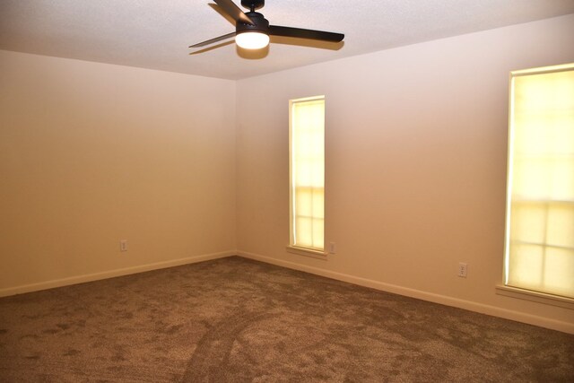 spare room with a ceiling fan, baseboards, and dark colored carpet