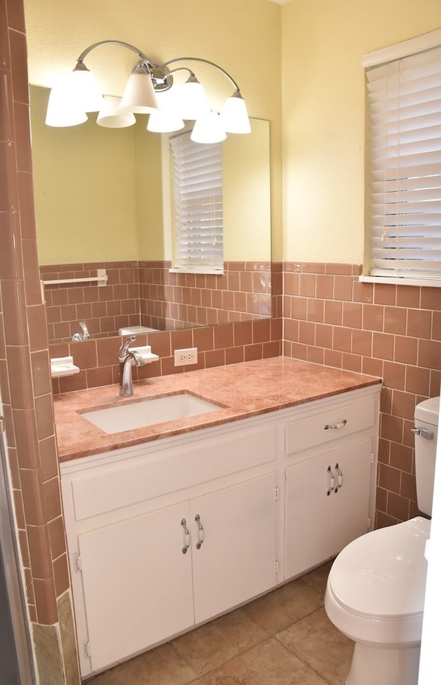 bathroom featuring a wainscoted wall, tile patterned floors, toilet, vanity, and tile walls