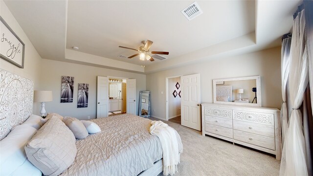 bedroom with a ceiling fan, light carpet, a raised ceiling, ensuite bath, and visible vents