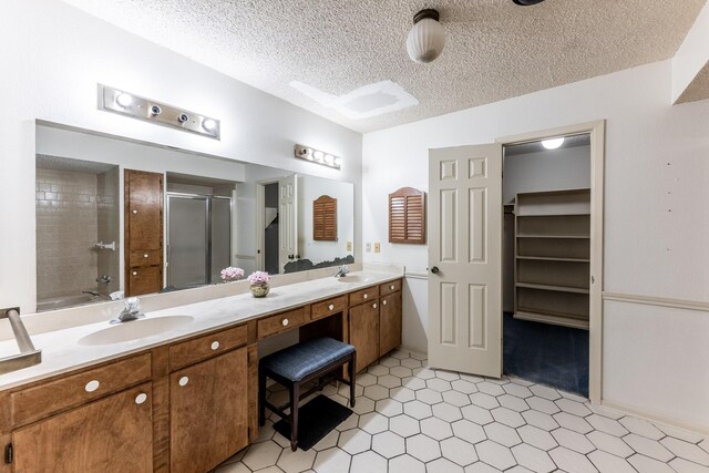 full bath featuring double vanity, a textured ceiling, a shower stall, and a sink
