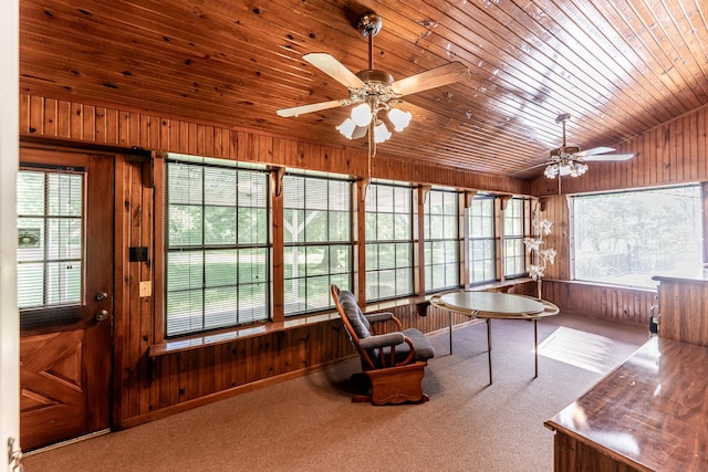 carpeted home office with wood walls, ceiling fan, plenty of natural light, and vaulted ceiling