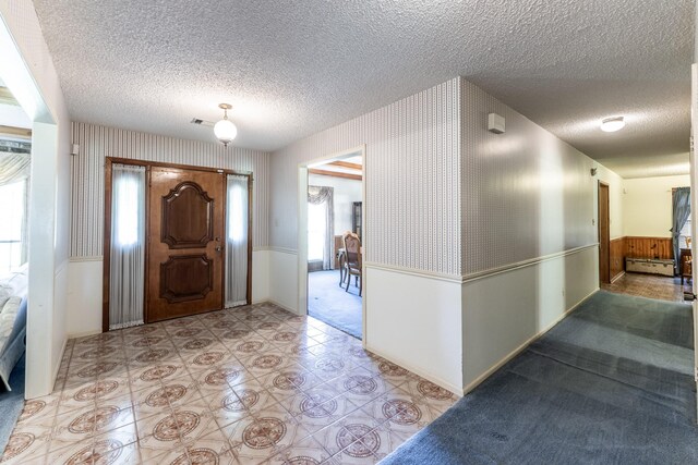 foyer featuring a wainscoted wall, baseboard heating, visible vents, a textured ceiling, and wallpapered walls