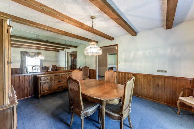dining space with beam ceiling, wooden walls, dark carpet, a textured ceiling, and wainscoting