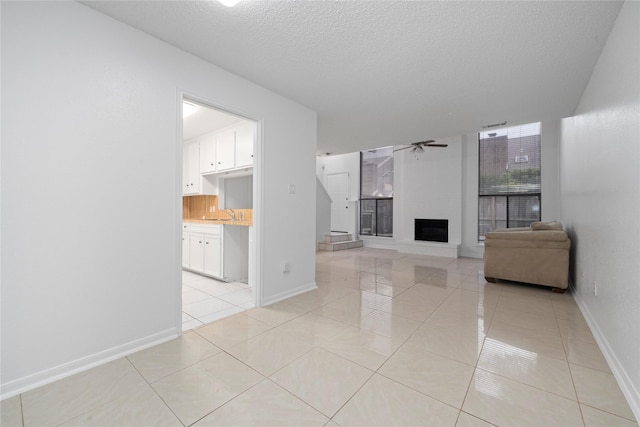 13742 Hollowgreen Dr Unit 604, Houston, TX 77082 - unfurnished living room featuring ceiling fan, a textured ceiling, a fireplace, light tile patterned floors, and baseboards