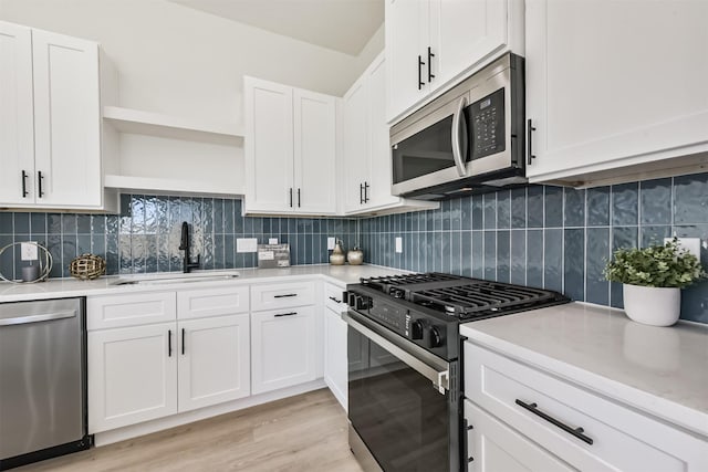 kitchen featuring appliances with stainless steel finishes, open shelves, a sink, light countertops, and white cabinets