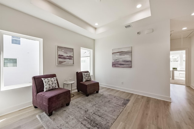 sitting room featuring visible vents, attic access, light wood-style flooring, and a tray ceiling