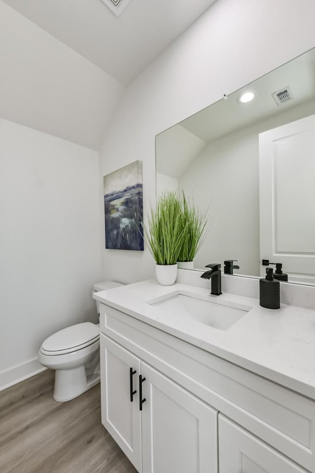 half bath featuring vanity, toilet, wood finished floors, lofted ceiling, and visible vents