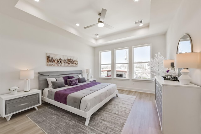 bedroom featuring recessed lighting, a tray ceiling, visible vents, and light wood-style floors