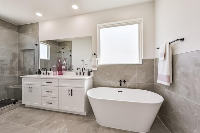 full bath featuring a freestanding bath, a sink, double vanity, tile walls, and a stall shower
