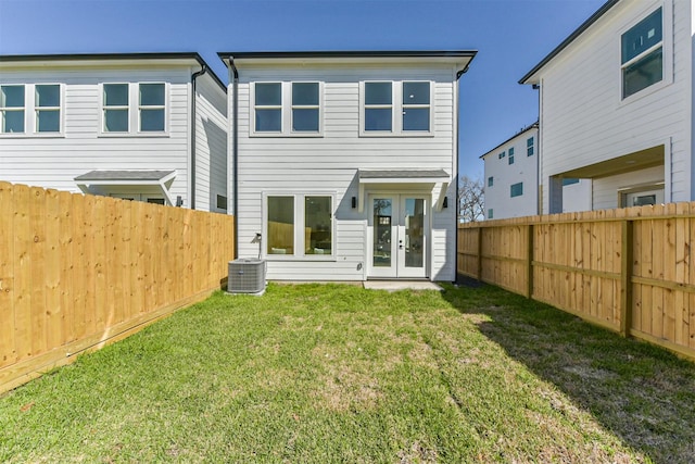back of property with a lawn, french doors, a fenced backyard, and central AC unit