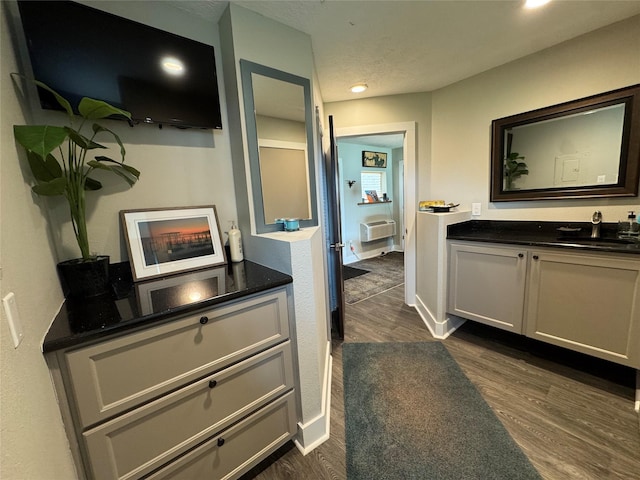 hallway with a wall unit AC, a sink, baseboards, dark wood-style floors, and recessed lighting