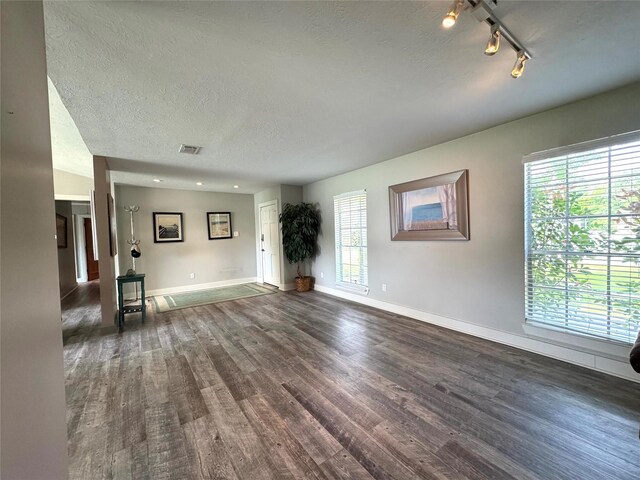 unfurnished living room with rail lighting, a textured ceiling, visible vents, dark wood-style flooring, and baseboards