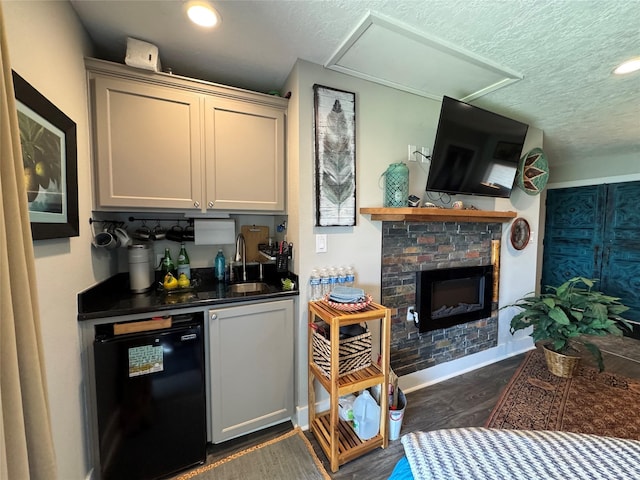bar featuring a sink, black dishwasher, a textured ceiling, dark wood-type flooring, and a glass covered fireplace