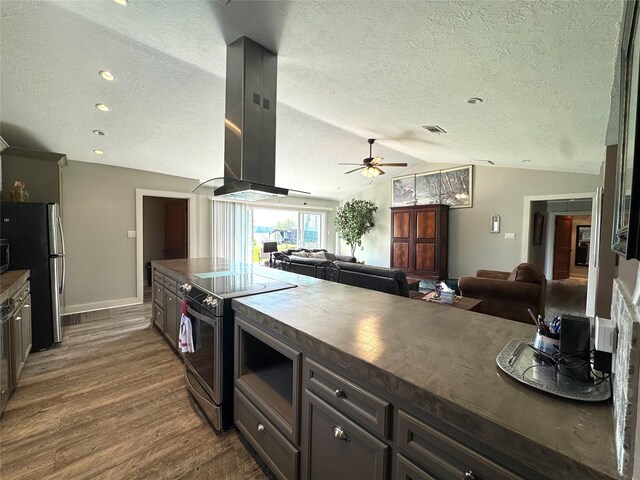 kitchen with dark countertops, island range hood, dark wood-type flooring, ceiling fan, and appliances with stainless steel finishes