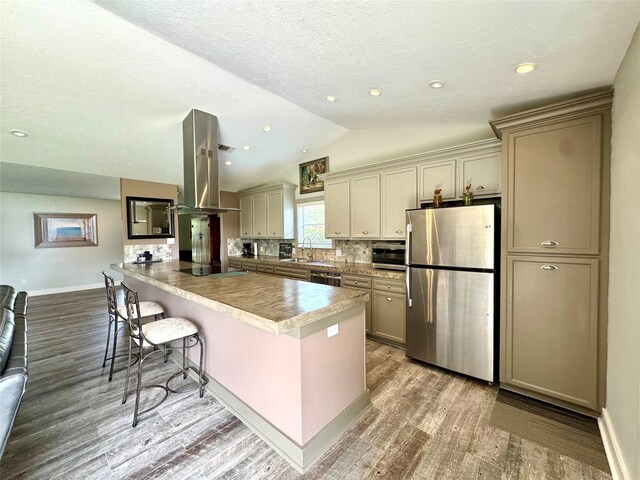 kitchen featuring wood finished floors, island exhaust hood, freestanding refrigerator, lofted ceiling, and black electric stovetop