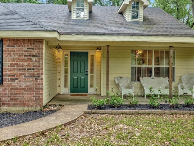 entrance to property featuring covered porch, brick siding, and a shingled roof