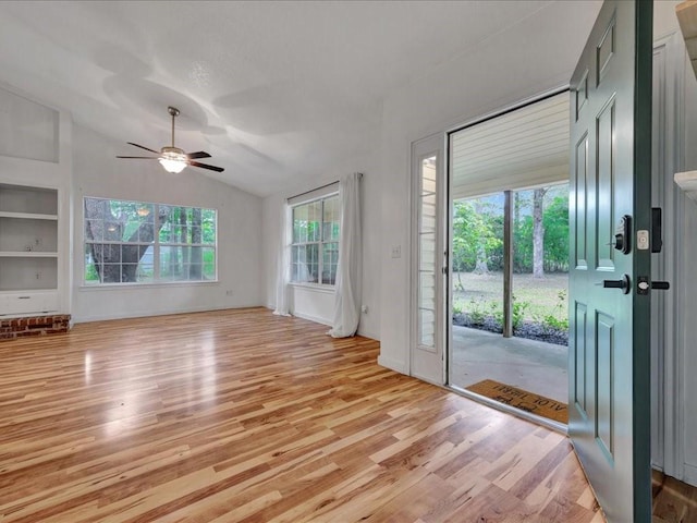 interior space featuring light wood-style floors, built in shelves, ceiling fan, vaulted ceiling, and baseboards