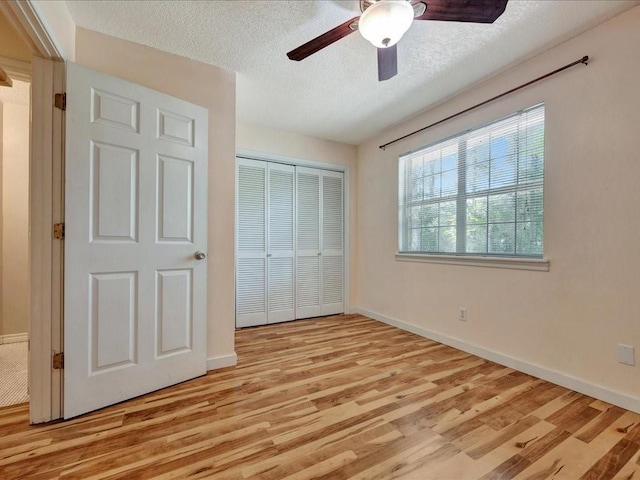unfurnished bedroom featuring baseboards, light wood-type flooring, a textured ceiling, and a closet
