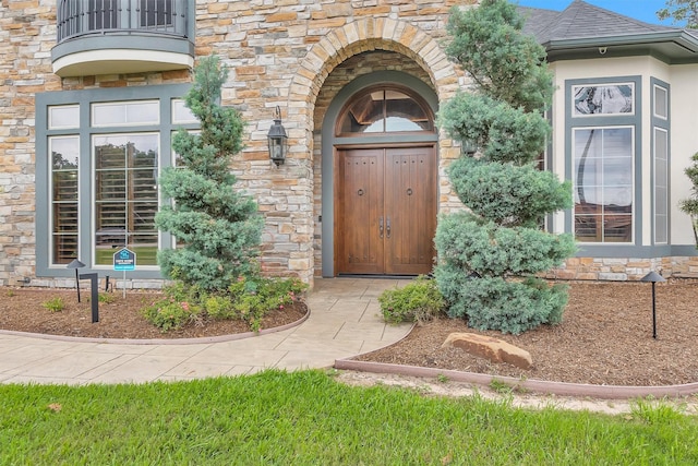 property entrance with a shingled roof, a balcony, and stone siding