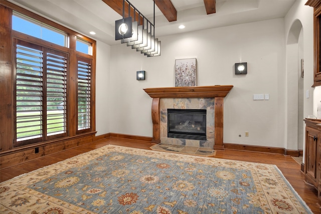 living area featuring beam ceiling, baseboards, wood finished floors, and a fireplace