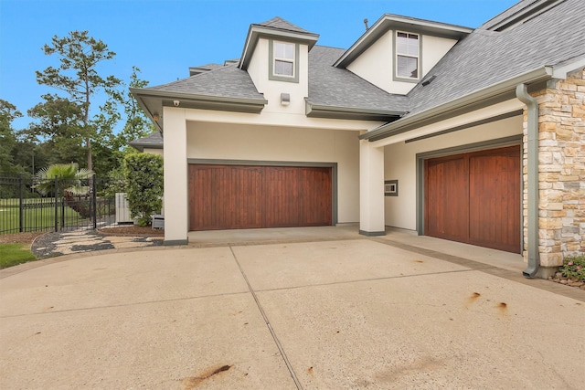 view of front of house with a shingled roof, an attached garage, stone siding, stucco siding, and driveway