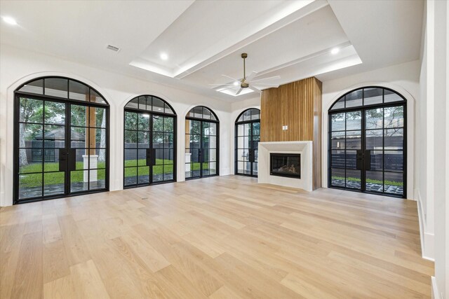 unfurnished living room featuring light wood-type flooring, french doors, a large fireplace, and ceiling fan