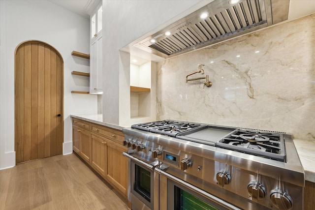 kitchen featuring open shelves, premium range hood, light wood-type flooring, range with two ovens, and tasteful backsplash