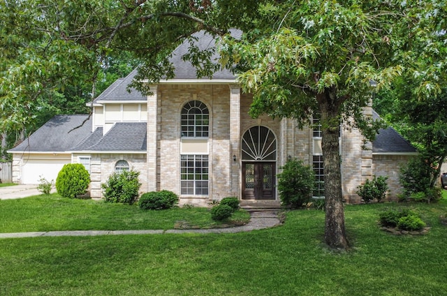traditional home featuring a front yard, roof with shingles, brick siding, concrete driveway, and an attached garage