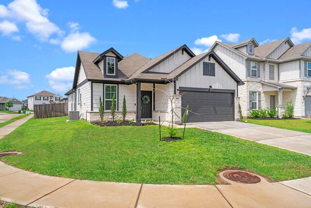 view of front of property featuring board and batten siding, fence, stone siding, a front lawn, and concrete driveway