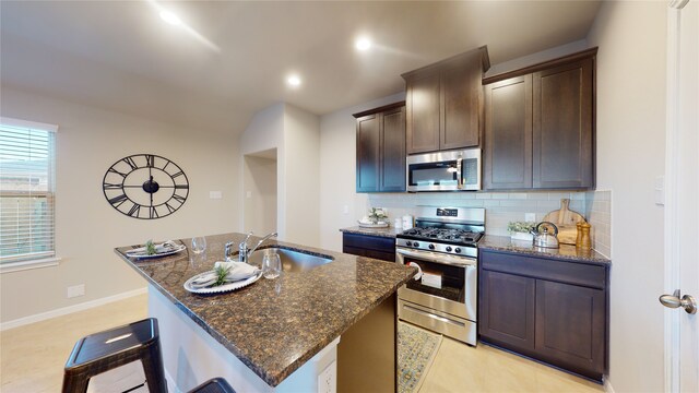 kitchen featuring a sink, appliances with stainless steel finishes, tasteful backsplash, and dark stone counters