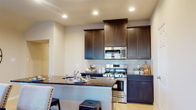 kitchen featuring dark brown cabinetry, a sink, dark stone countertops, appliances with stainless steel finishes, and backsplash