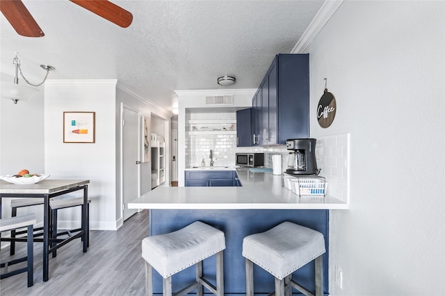 6300 Seawall Blvd Unit 3225, Galveston, TX 77551 - kitchen with stainless steel microwave, crown molding, blue cabinetry, and decorative backsplash