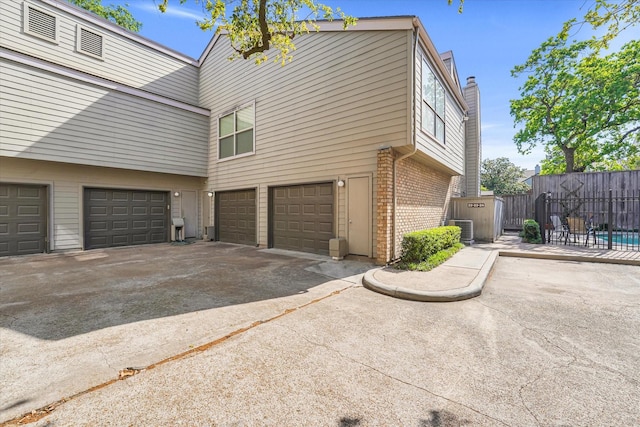 view of property exterior with central AC, a chimney, concrete driveway, an attached garage, and brick siding
