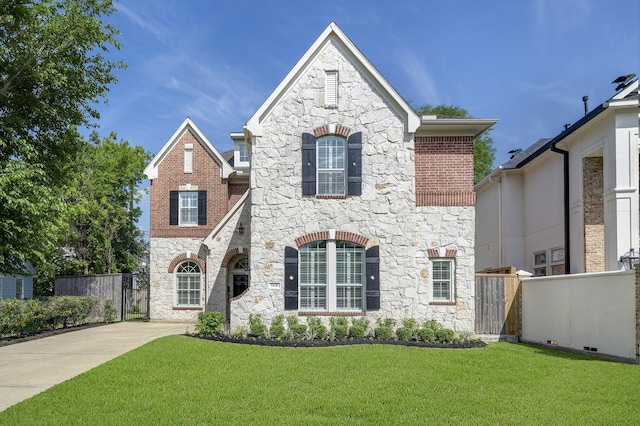 french provincial home featuring a front yard, stone siding, and fence