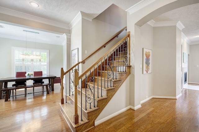 stairway featuring arched walkways, ornamental molding, wood finished floors, and baseboards