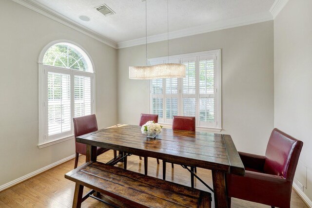 dining space with visible vents, light wood-type flooring, crown molding, and baseboards