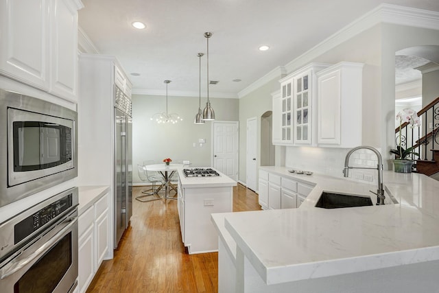 kitchen featuring built in appliances, arched walkways, a sink, and light wood-style flooring